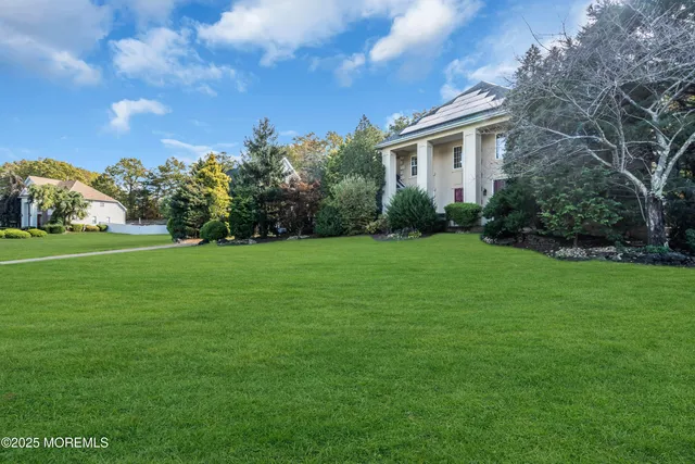 a view of a white house in front of a big yard with plants and large trees