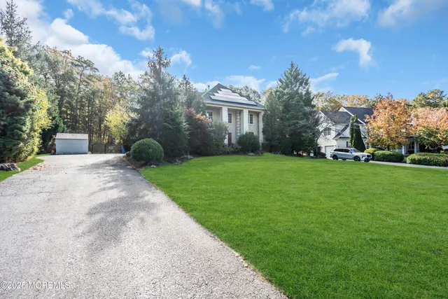a view of a white house in front of a big yard with plants and large trees