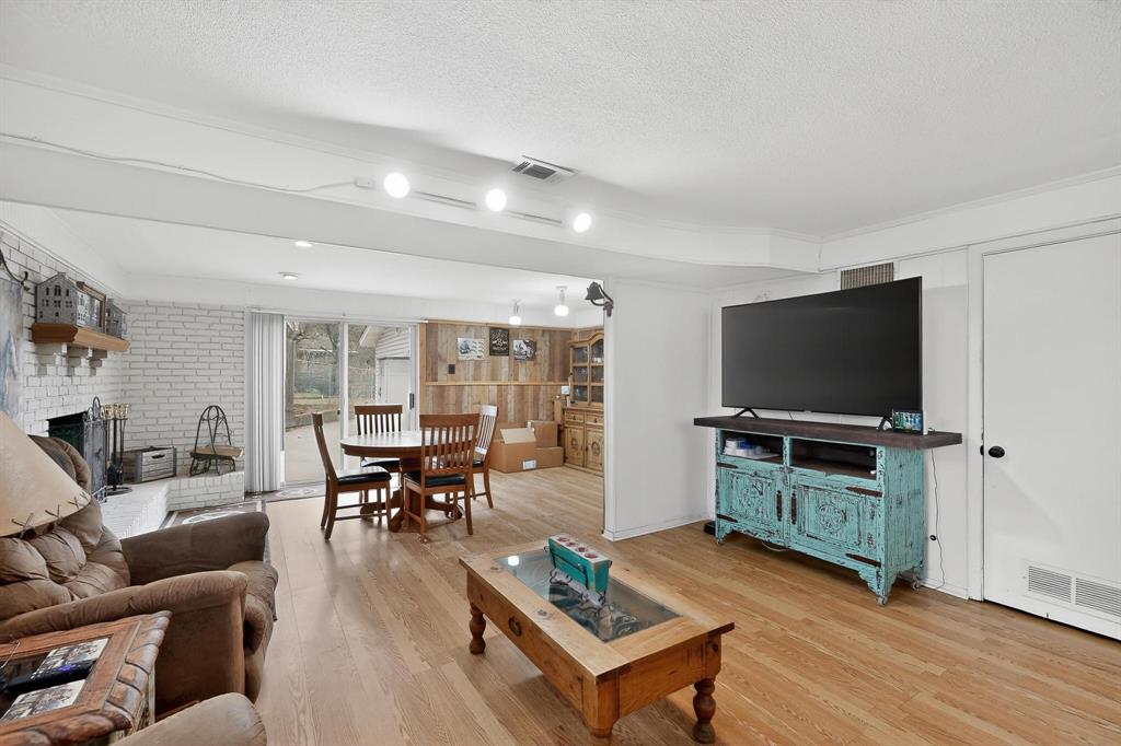 202 Senter Valley Road Irving, TX 75060 - Photo 5 of 32 Spacious living area featuring light wood-finish flooring, a painted brick fireplace with a wood mantel, and sliding glass doors providing outdoor access