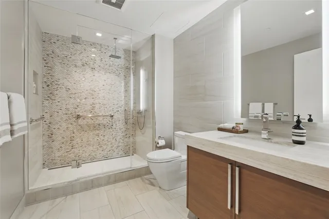 a bathroom with a granite countertop sink a toilet a mirror and shower