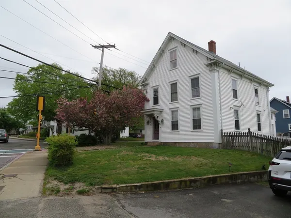 a view of a white house next to a yard with big trees