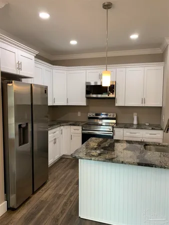 a view of a kitchen with kitchen island stainless steel appliances a sink dishwasher a stove and a dining table with wooden floor