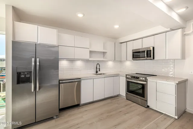 a kitchen with stainless steel appliances granite countertop a refrigerator a stove a sink and white cabinets