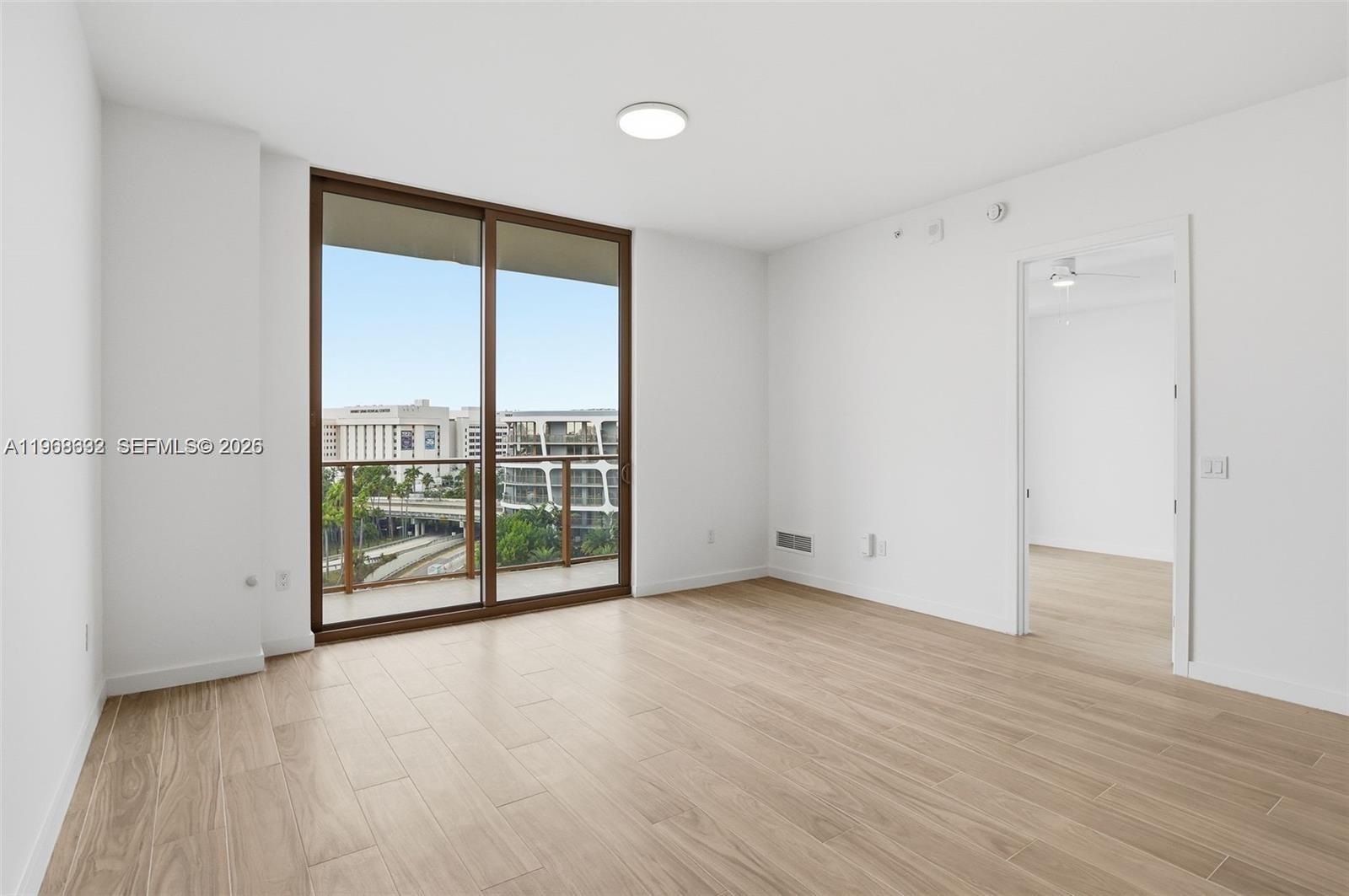 3900 Alton Road, Unit 208 Miami Beach, FL 33140 - Photo 12 of 26 a view of an empty room with wooden floor and sliding glass door