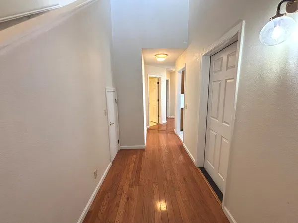 a view of a hallway with wooden floor and a bathroom