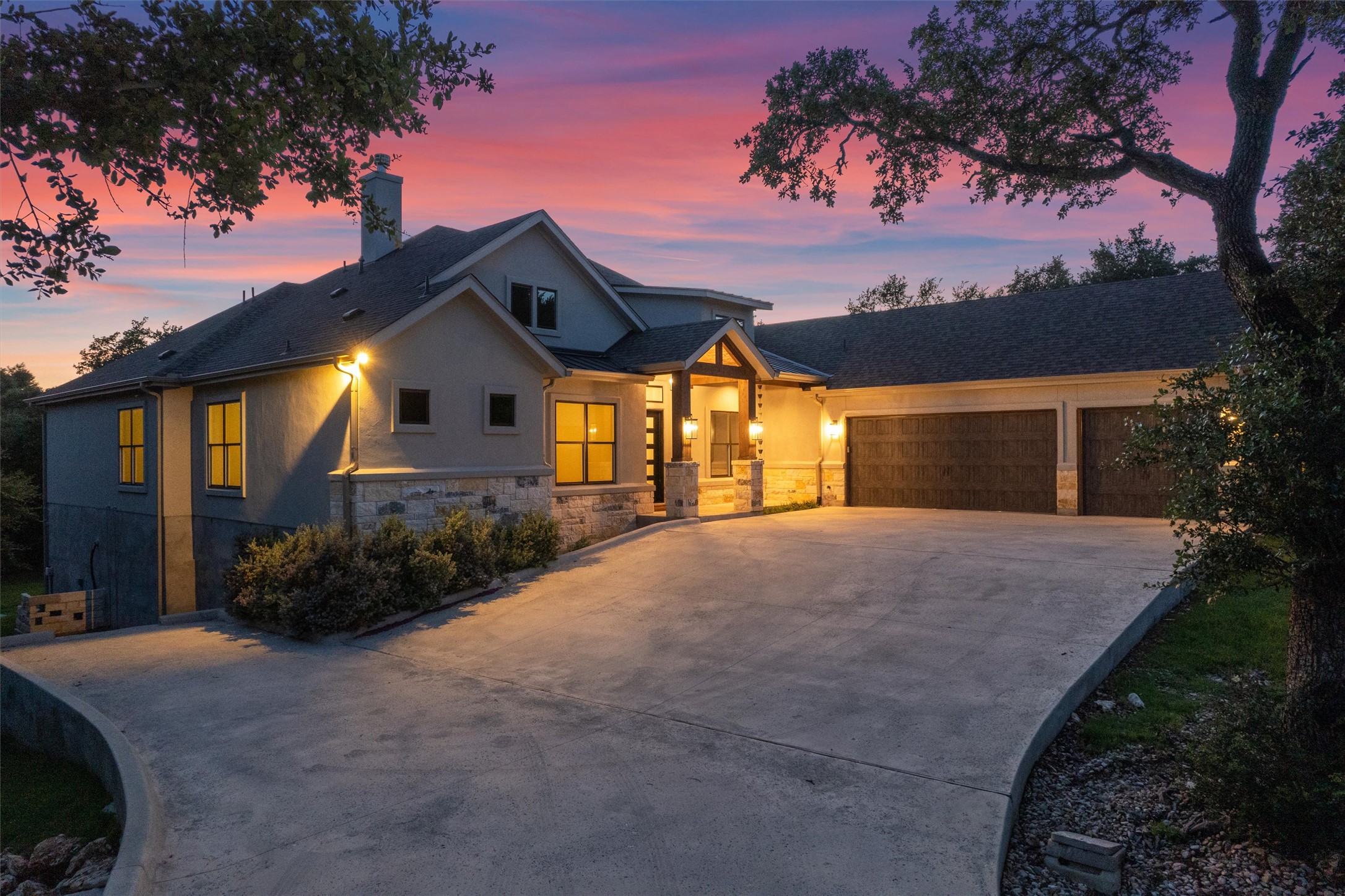 302 Highland Spring Lane Georgetown, TX 78633 - Photo 5 of 38 A striking modern facade with stone and stucco accents illuminates the expansive driveway and three-car garage at twilight.