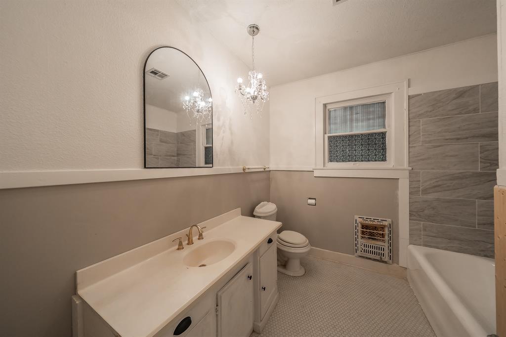 1500 Proctor Avenue Waco, TX 76708 - Photo 34 of 40 Bathroom featuring a vanity with a white countertop and gold-toned faucet, a wall-mounted mirror, a toilet, a bathtub, and tiled walls in the shower area