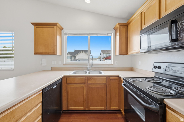 2575 Athena Drive Magna, UT 84044 - Photo 8 of 23 Kitchen featuring wood-finish cabinetry, light-toned countertops, a stainless steel double basin sink with a chrome faucet, and integrated black appliances including a range and microwave