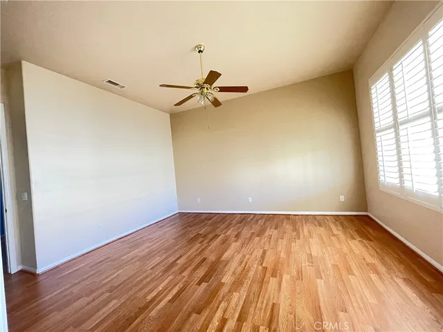 an empty room with wooden floor fan and windows