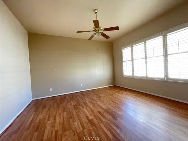 an empty room with wooden floor fan and windows