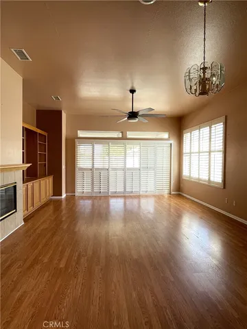 an empty room with wooden floor chandelier and windows