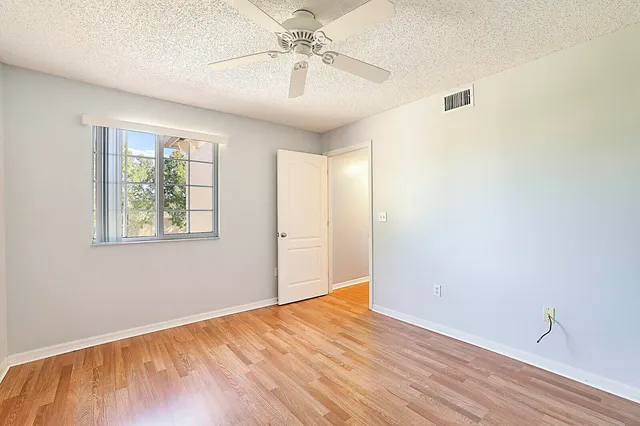 an empty room with wooden floor chandelier fan and windows