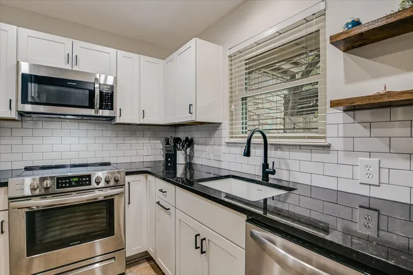 a kitchen with granite countertop white cabinets stainless steel appliances and a sink