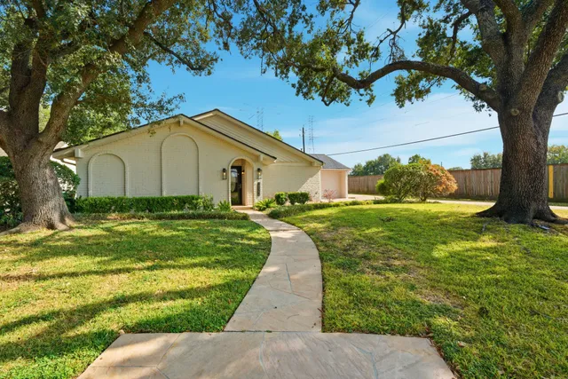 a white house with a big yard plants and large trees