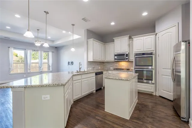 a kitchen with stainless steel appliances granite countertop a refrigerator a sink dishwasher a stove and white cabinets with wooden floor