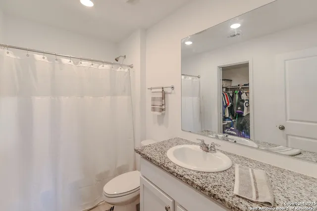 a bathroom with a granite countertop sink a toilet a mirror and shower curtain
