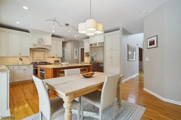 a kitchen with stainless steel appliances granite countertop a stove a refrigerator a kitchen island a sink and a dining table with wooden floor