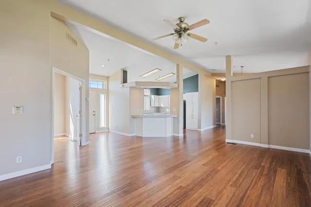 a view of an empty room with wooden floor and a ceiling fan