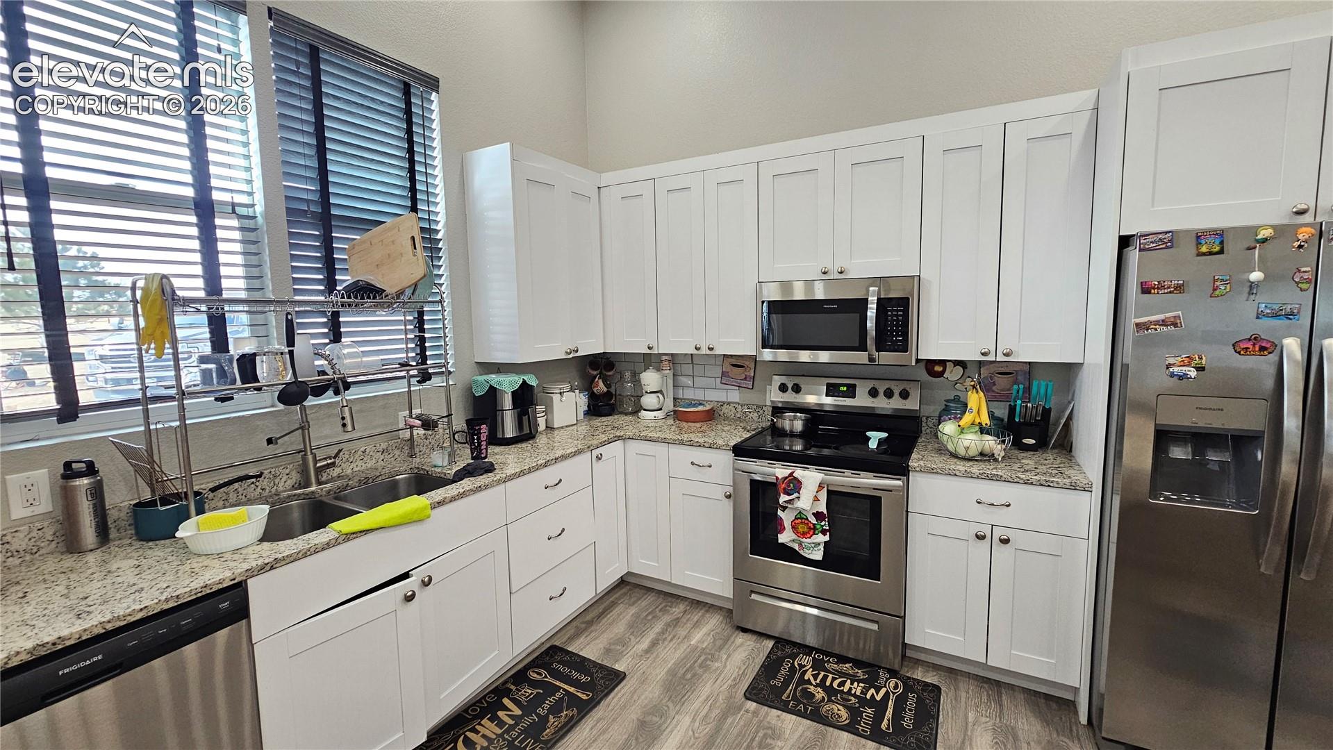 3835 Sengbeil Road Yoder, CO 80864 - Photo 13 of 48 Modern kitchen featuring white shaker cabinetry, stainless steel appliances, speckled stone countertops, a double basin sink, and wood-finish flooring