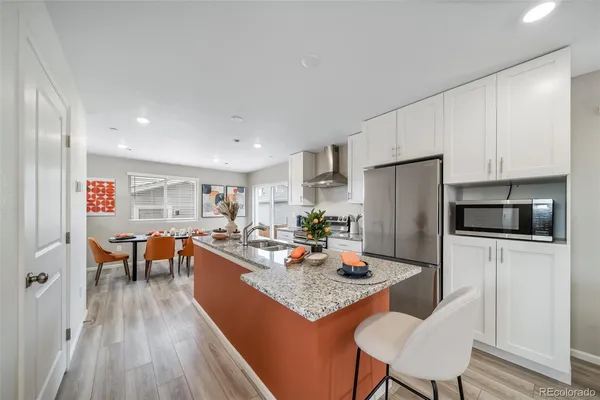 a kitchen with stainless steel appliances granite countertop a refrigerator a stove a sink a dining table and chairs with wooden floor