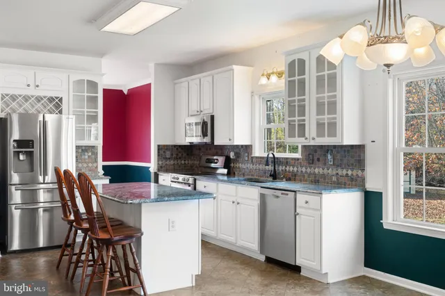 a kitchen with stainless steel appliances granite countertop a stove top oven a sink dishwasher and white cabinets with wooden floor