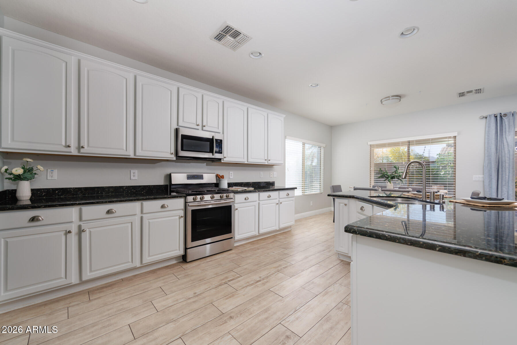 3167 East Powell Way Gilbert, AZ 85298 - Photo 8 of 39 a large white kitchen with granite countertop a stove a sink a window and white cabinets
