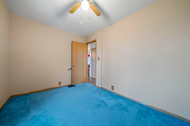 an empty room with a chandelier fan and wooden floor