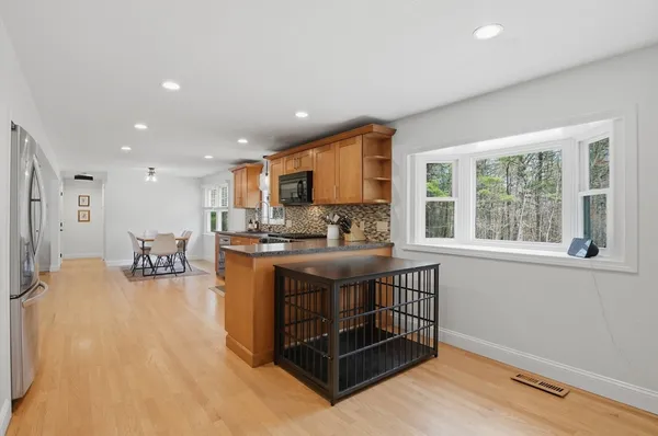 a kitchen with stainless steel appliances granite countertop a stove a sink a refrigerator and a dining table with wooden floor