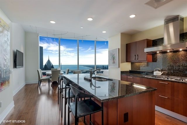 a kitchen with stainless steel appliances granite countertop a refrigerator a sink a stove a dining table and chairs