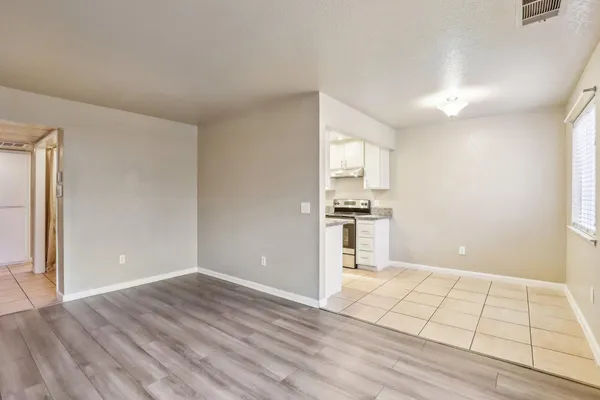 a view of an empty room with kitchen and window