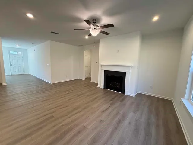 an empty room with wooden floor a ceiling fan a fireplace and windows