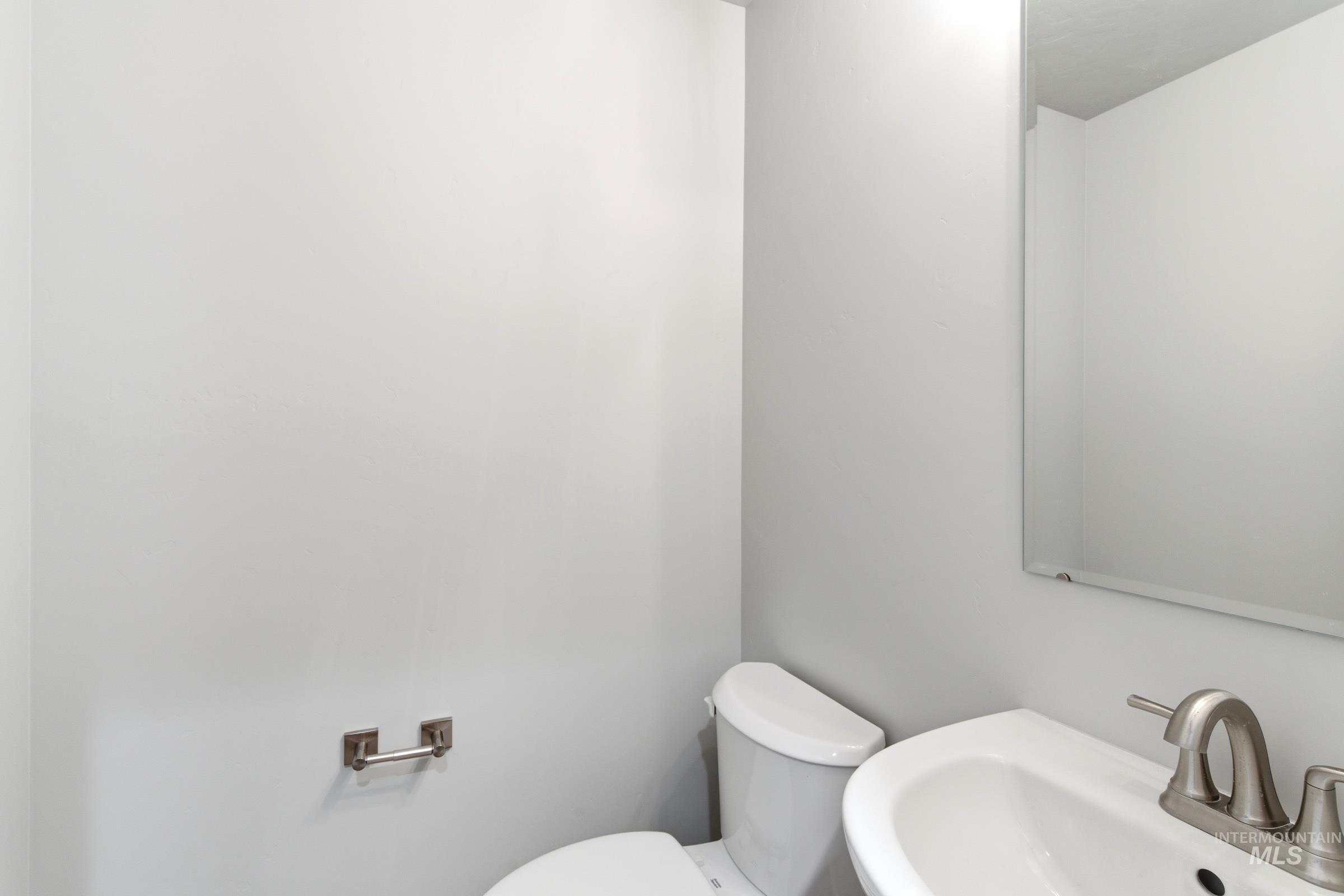 2374 West Fallon Loop Nampa, ID 83651 - Photo 13 of 24 Powder room featuring a wall-mounted mirror, ceramic sink, brushed nickel faucet, and a toilet with a white tank and bowl