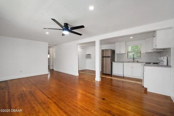 a view of an empty room with kitchen appliances and a ceiling fan