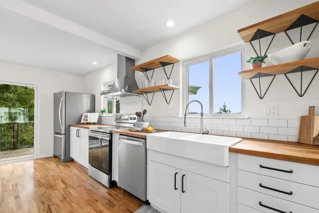 a large kitchen with stainless steel appliances granite countertop a refrigerator a stove a sink dishwasher and white cabinets with wooden floor