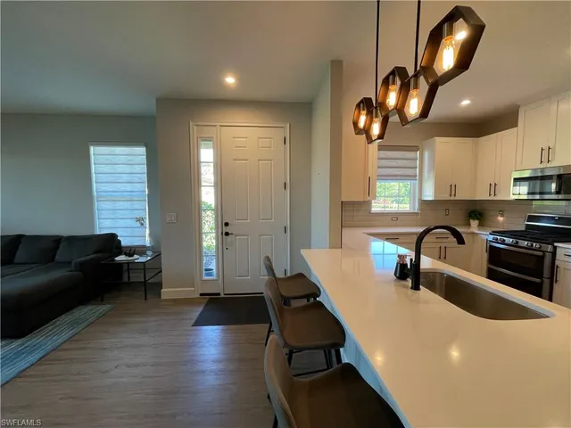 a kitchen with granite countertop a stove a sink a refrigerator and blue cabinets with wooden floor