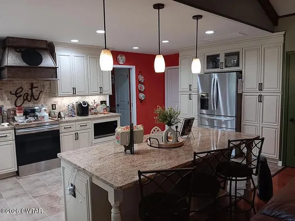 a kitchen with granite countertop a stove a refrigerator and a dining table with wooden floor