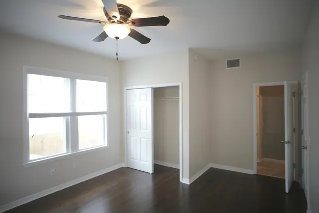 an empty room with wooden floor ceiling fan and windows