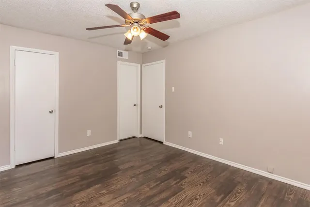 an empty room with wooden floor fan and windows