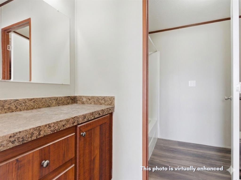 2722 Denver Road Sunset, TX 76270 - Photo 15 of 19 Bathroom vanity featuring wood-finish cabinetry, a speckled countertop, and a wall-mounted mirror