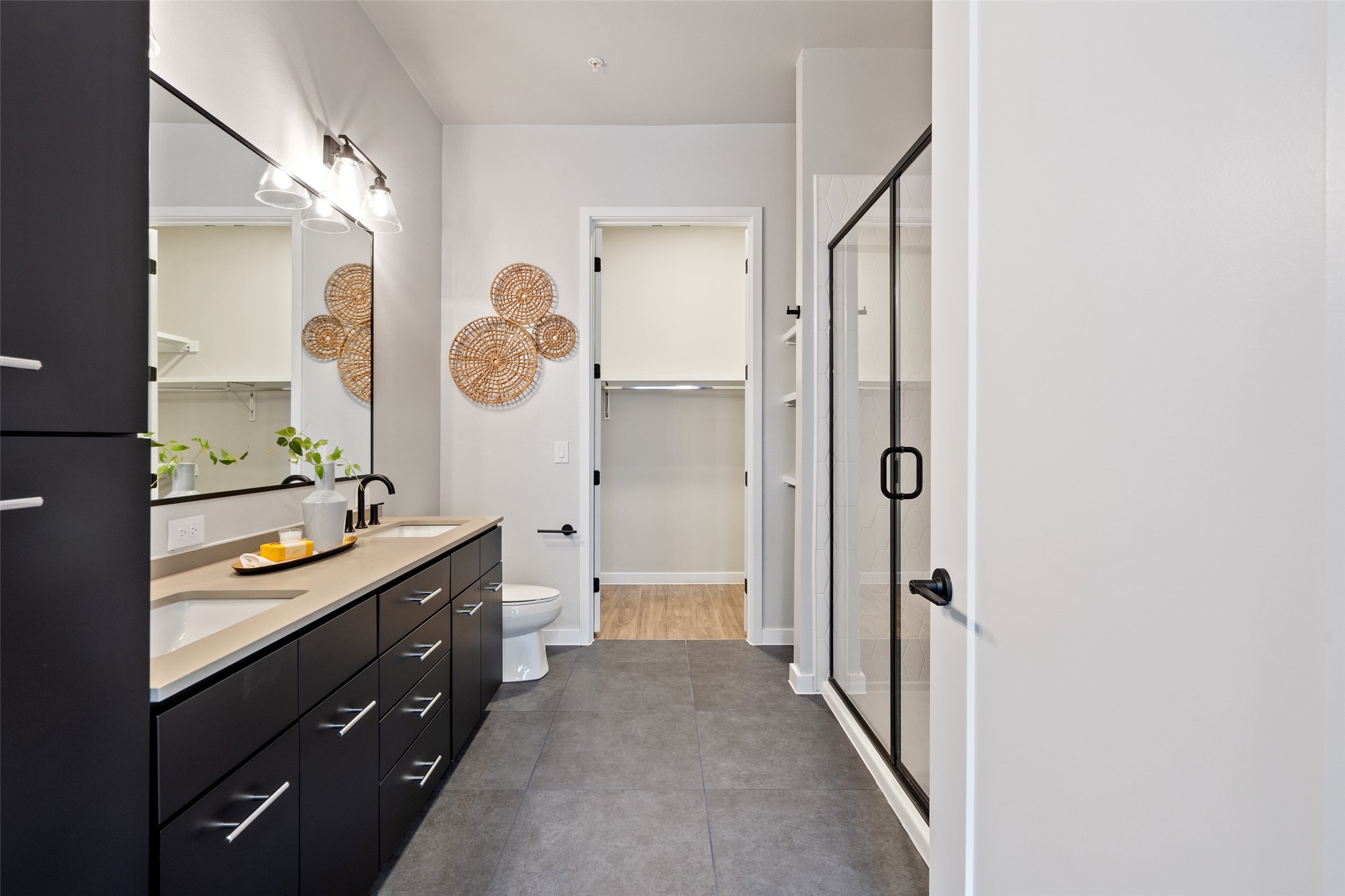 4510 Terry-O Lane, Unit 341 Austin, TX 78745 - Photo 28 of 40 Bathroom featuring a dark wood double vanity with dual sinks, a large mirror with overhead lighting, a glass-enclosed shower, and dark tile flooring