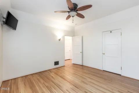a view of an empty room with wooden floor and a ceiling fan