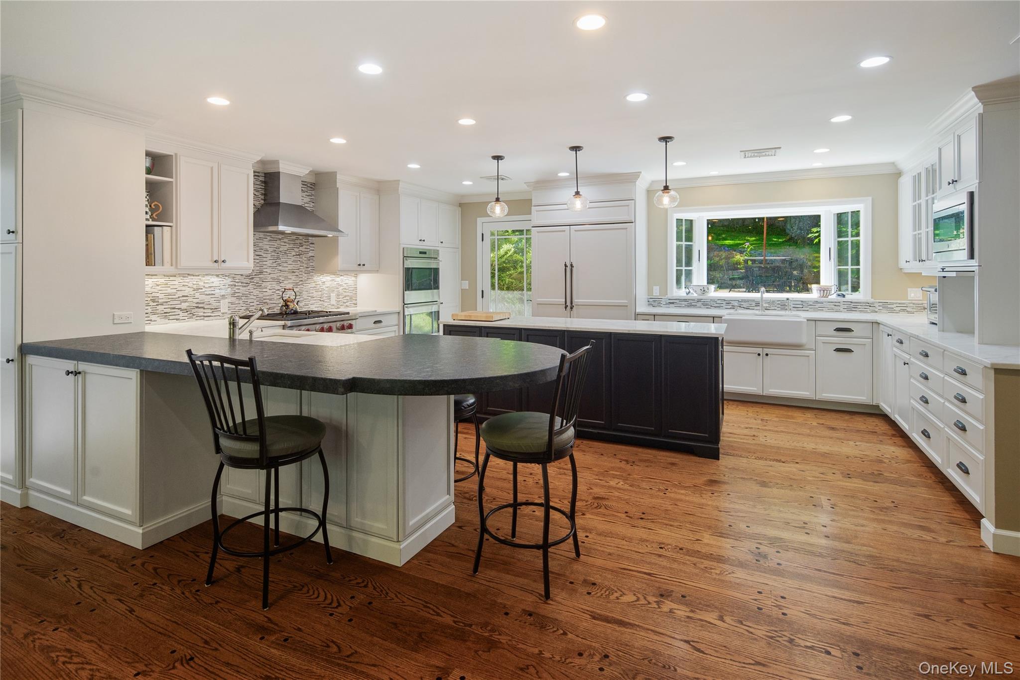 105 Cross Ridge Road Chappaqua, NY 10514 - Photo 13 of 43 The renovated kitchen features both a seating peninsula and a center island, honed granite and Carrera marble counters, sparkling white soft close cabinetry with interior pullouts, a Shaw farmhouse sink and addt'l prep sink, a large Subzero and Bosch dishwasher with integral door panels, stainless steel Wolf convection double wall ovens and Wolf 6 burner gas cooktop, an appliance garage, pendant and recessed lighting, a large bay window overlooking the back patios and yard, glazed display cabinets, cookbook shelves, a built-in microwave, wide board pegged oak floors, a large walk-in pantry, and a door out to the patio.