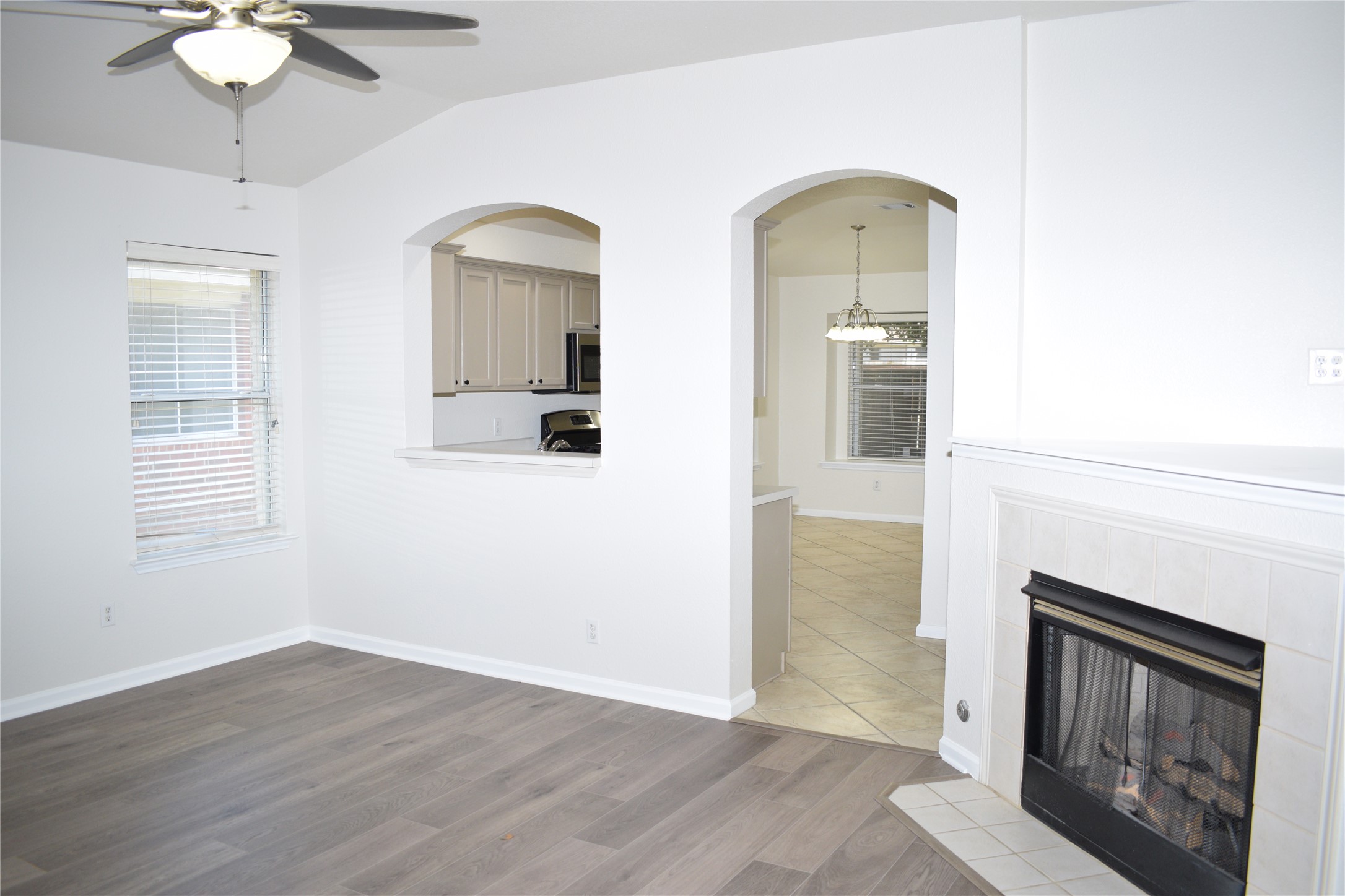 3209 Port Anne Way Leander, TX 78641 - Photo 9 of 30 Interior space featuring wood-finish flooring, a fireplace with a tile surround and hearth, a ceiling fan with integrated lighting, and an arched passthrough to a kitchen with light-colored cabinetry