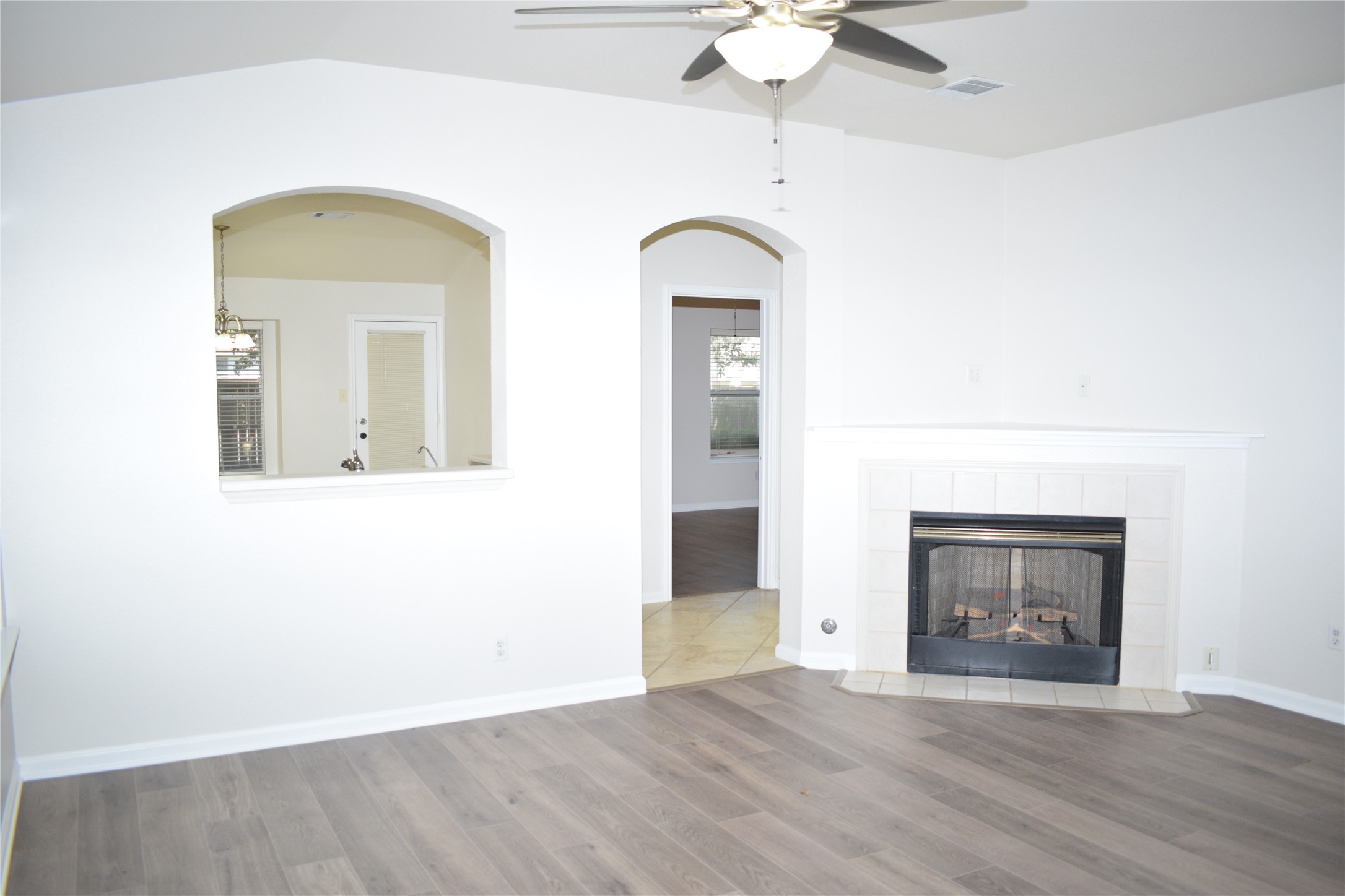 3209 Port Anne Way Leander, TX 78641 - Photo 10 of 30 Living area featuring wood-finish flooring, a tile-surround fireplace with hearth, an arched pass-through window, and a ceiling fan with integrated lighting