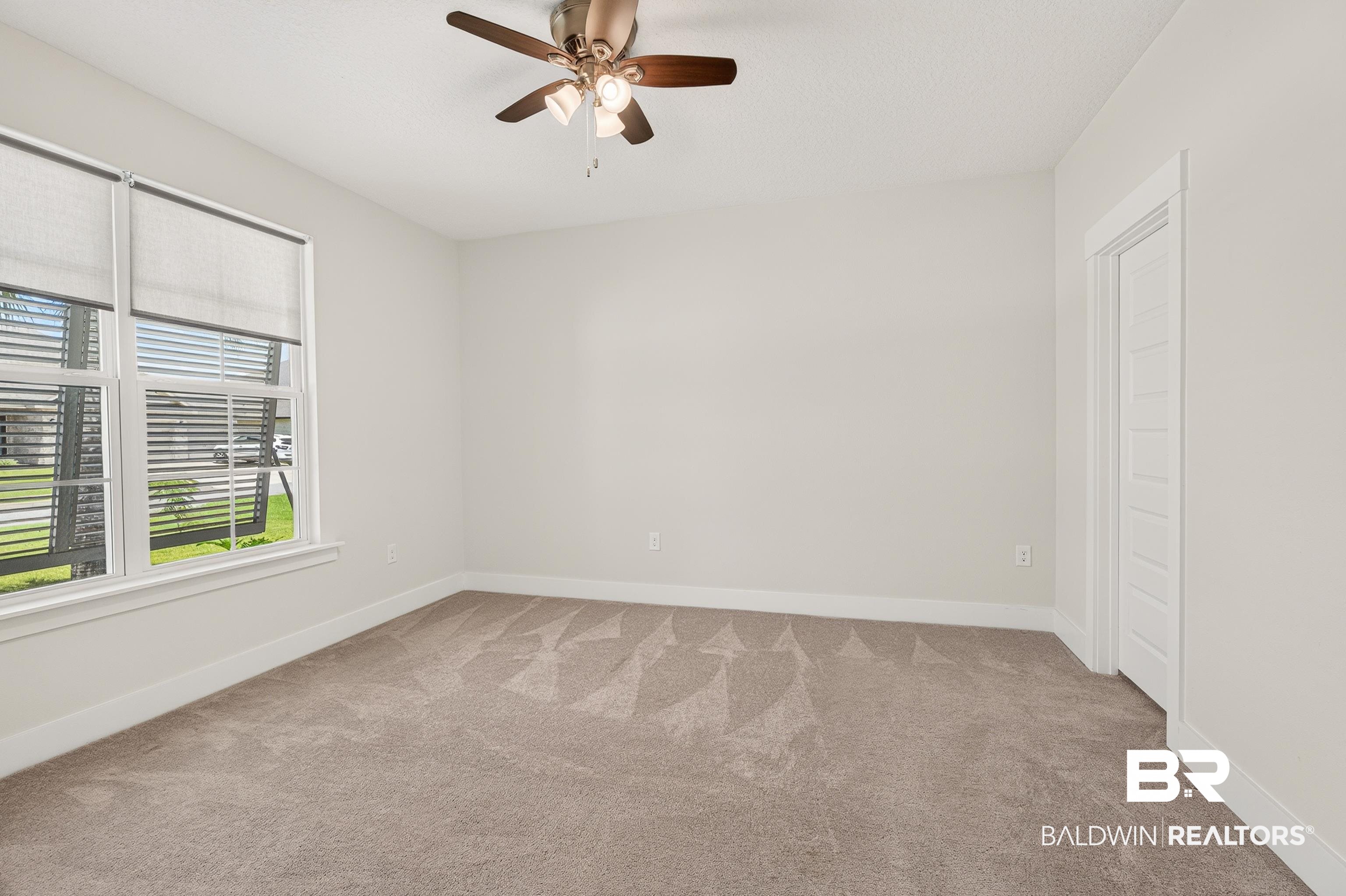 1724 Partridge Street Foley, AL 36535 - Photo 42 of 62 Neutral-toned room featuring broadloom carpeting, a window with roller shades and horizontal blinds, a ceiling fan with integrated lighting, and a paneled door with white trim