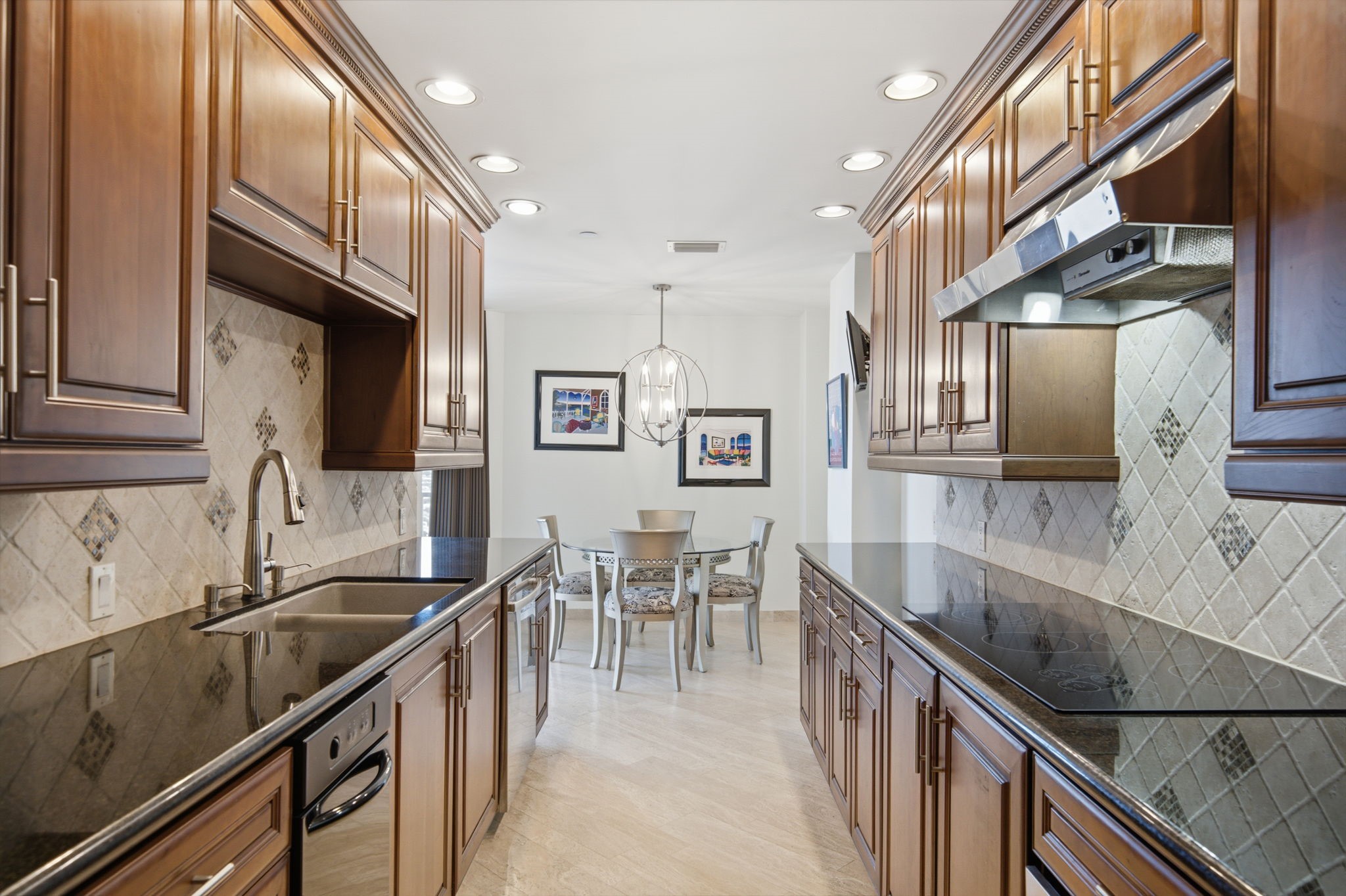 3350 McCue Road, Unit 2402 Houston, TX 77056 - Photo 23 of 49 Polished granite countertops line both sides of this sophisticated galley kitchen, complemented by classic raised-panel cabinetry and a decorative stone-patterned tile backsplash. The smooth-top cooktop and stainless vent hood blend seamlessly into the layout, leading directly toward an inviting casual breakfast area illuminated by a stylish globe pendant.