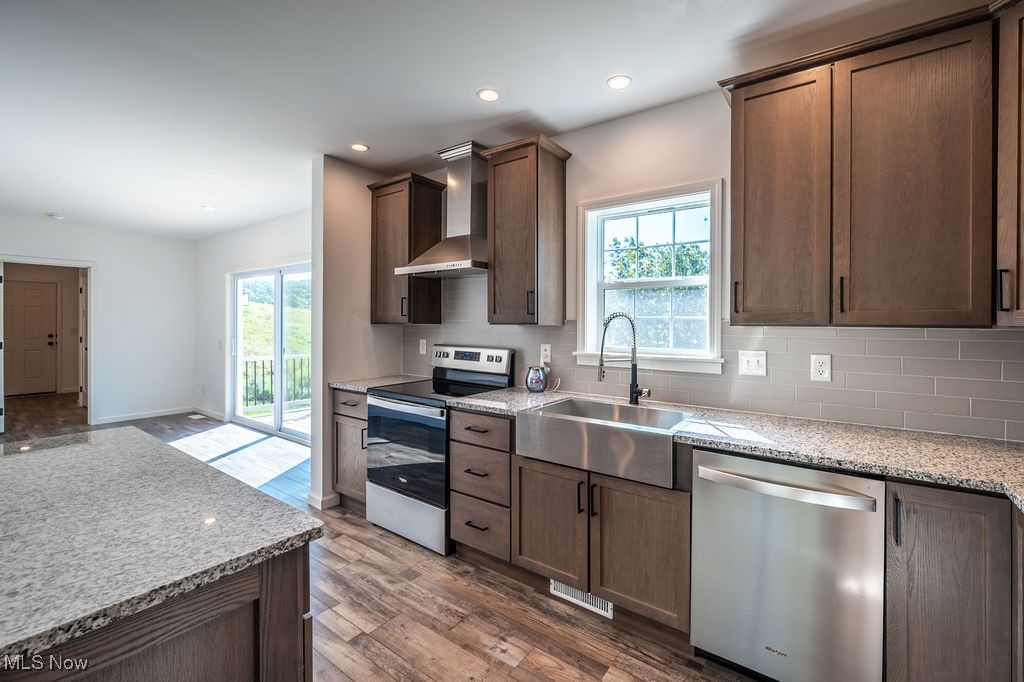 7343 Lost Pavement Road Belleville, WV 26133 - Photo 9 of 49 Kitchen with light stone counters, stainless steel appliances, backsplash, wall chimney range hood, and dark wood-type flooring