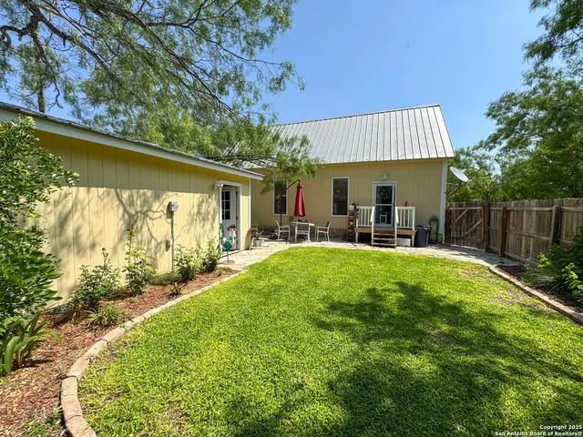a view of a backyard with table and chairs potted plants and large tree