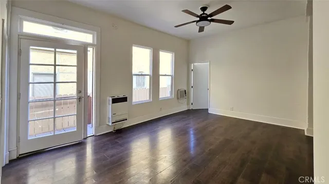 an empty room with wooden floor fan and windows