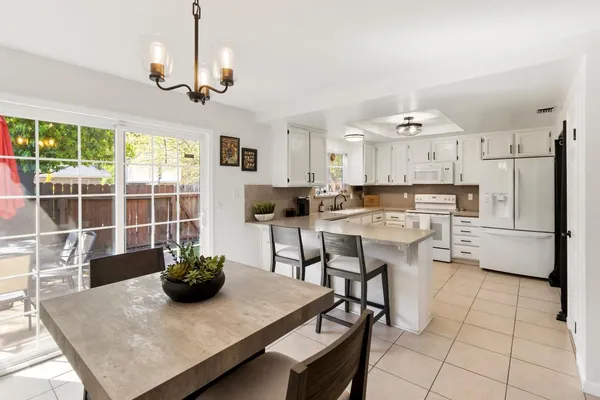 a kitchen with stainless steel appliances granite countertop a stove a refrigerator a sink a dining table and chairs with wooden floor